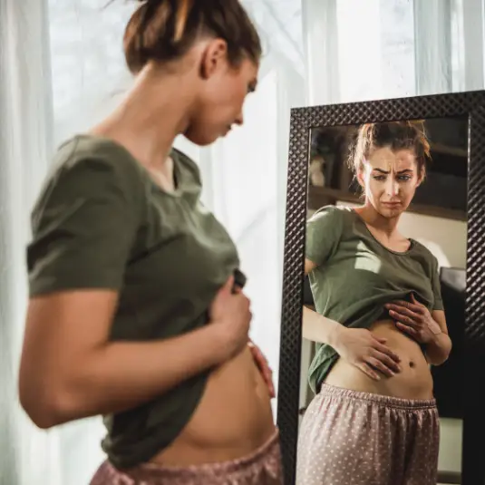 bloating Woman looks in mirror with bloated stomach